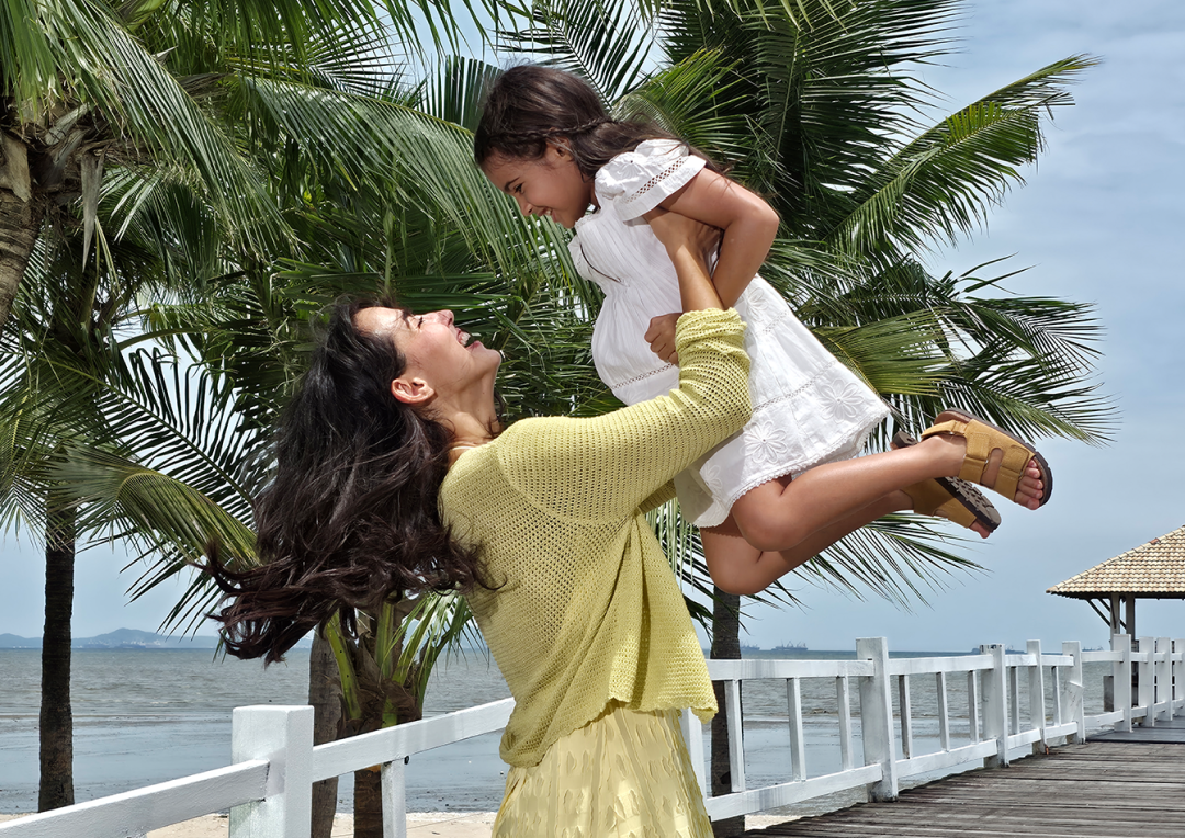 Detailed picture of a woman in a yellow outfit lifting a young girl in a white dress into the air